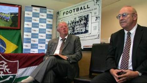 Dirigentes do Exeter fazem o an&uacute;ncio ao lado da bandeira do Flu