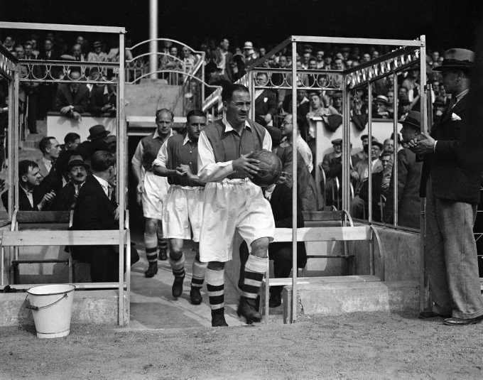 Alex James, capit&atilde;o do Arsenal, lidera os Gunners na entrada em campo para um jogo com o Everton na temporada 1936/37