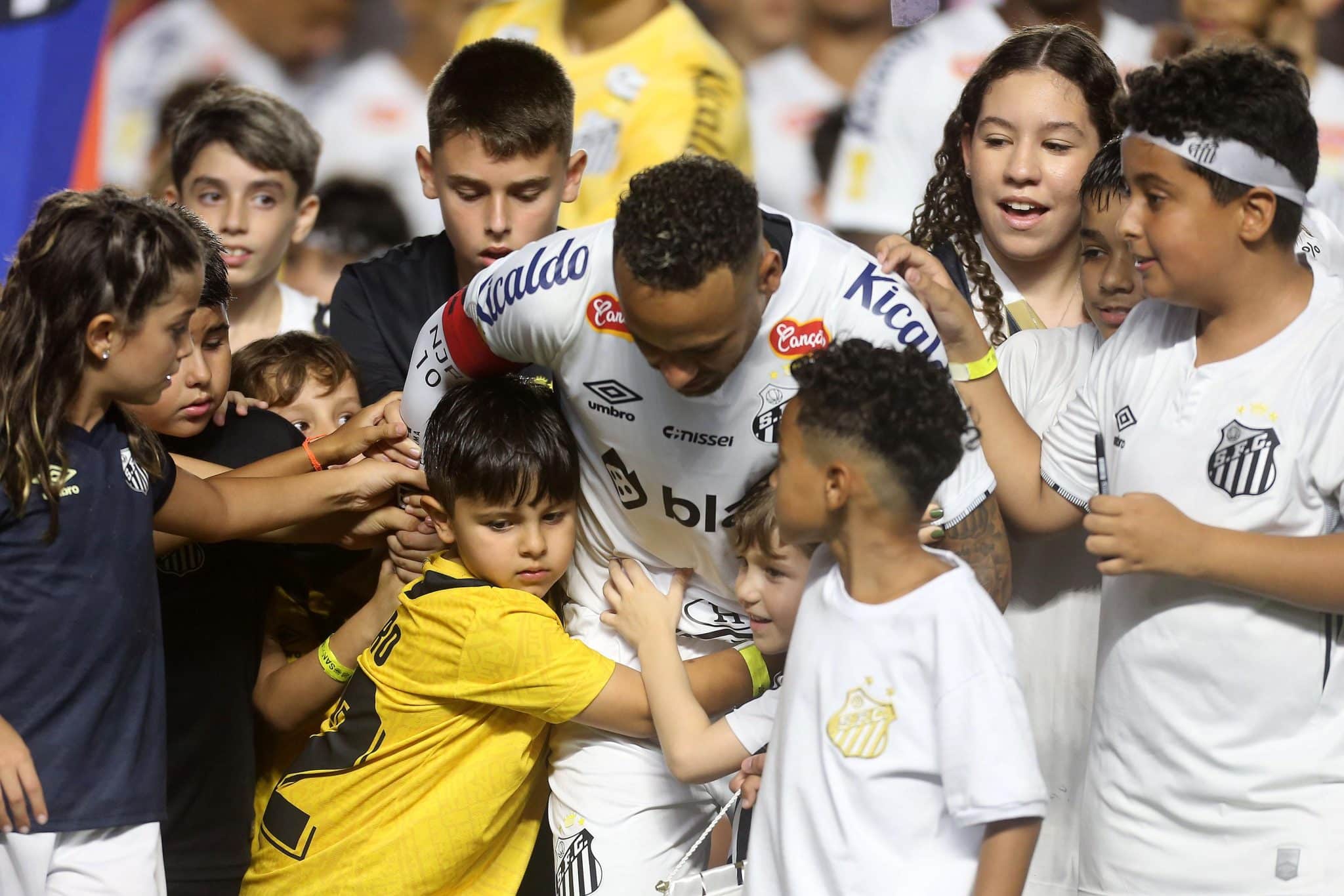 Neymar chega para o jogo no campo da Vila Belmiro cercado por garotos 