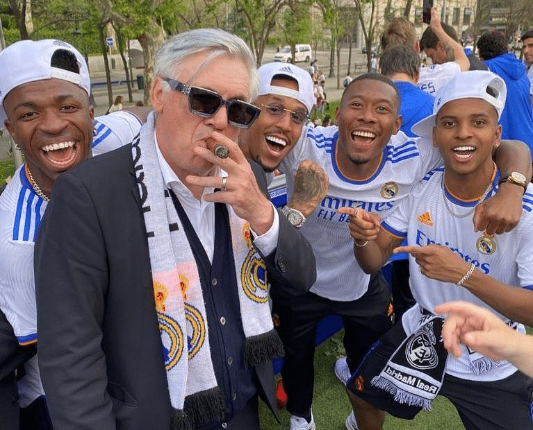 Com charuto na boca, Ancelotti comemora o t&iacute;tulo da Champions League de 2022 ao lado de Vinicius J&uacute;nior, Milit&atilde;o, Alaba e Rodrygo